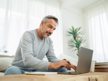 Confident Bearded mature adult man using and typing on laptop, Working at home office, Remote working, freelancer